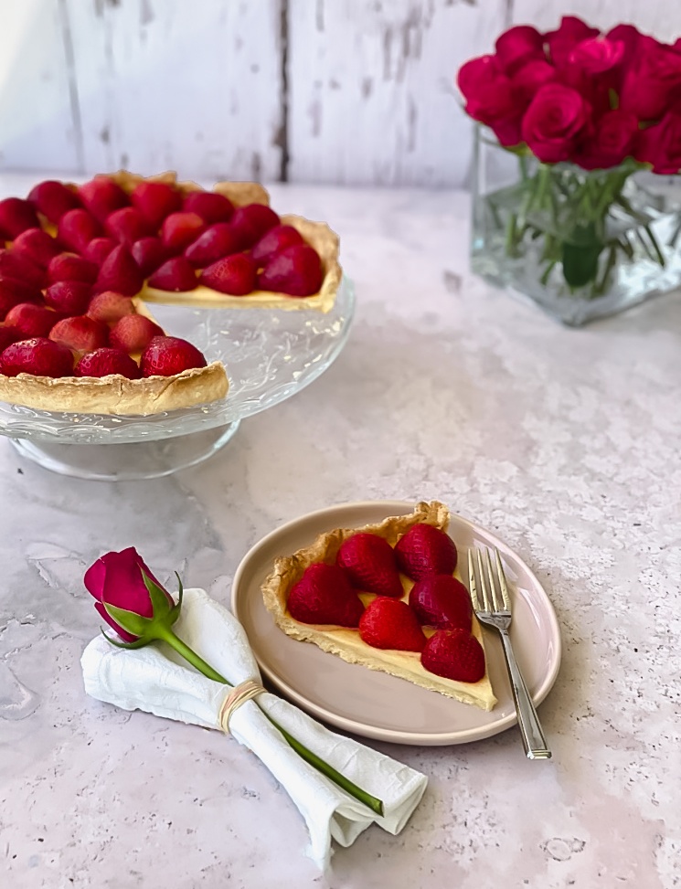 Strawberry Tart on cake stand with a plate and one slice and red roses.