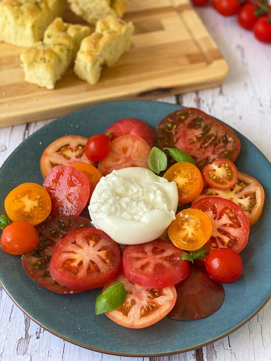 Heirloom Tomatoes and Burrata on blue plate with focaccia and tomato in background
