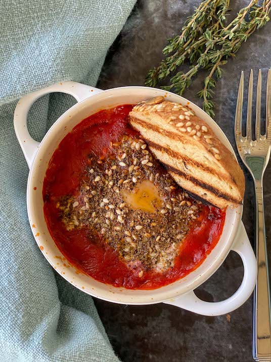 Eggs in a small bowl with tomato sauce and bread