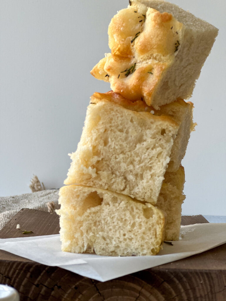 Rosemary focaccia bread squares overlapping in a tower over a wood tray.