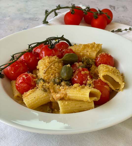 Cherry Tomato Pasta with capers and breadcrumbs on a mat with vine tomatoes on the background
