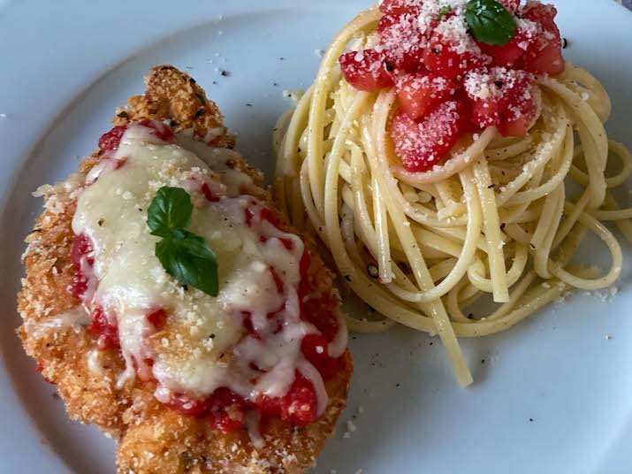 Crispy Chicken Parm on a plate with a side of spaghetti and fresh tomatoes.