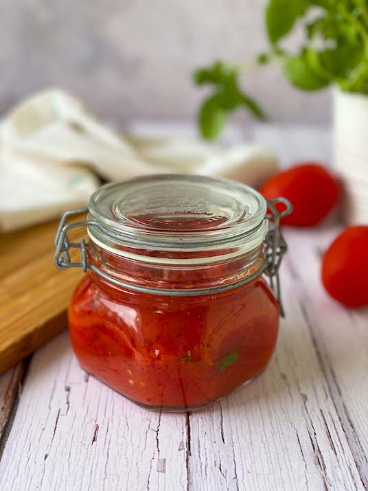 Jar of homemade Tomato Sauce canned over a table with basil plant