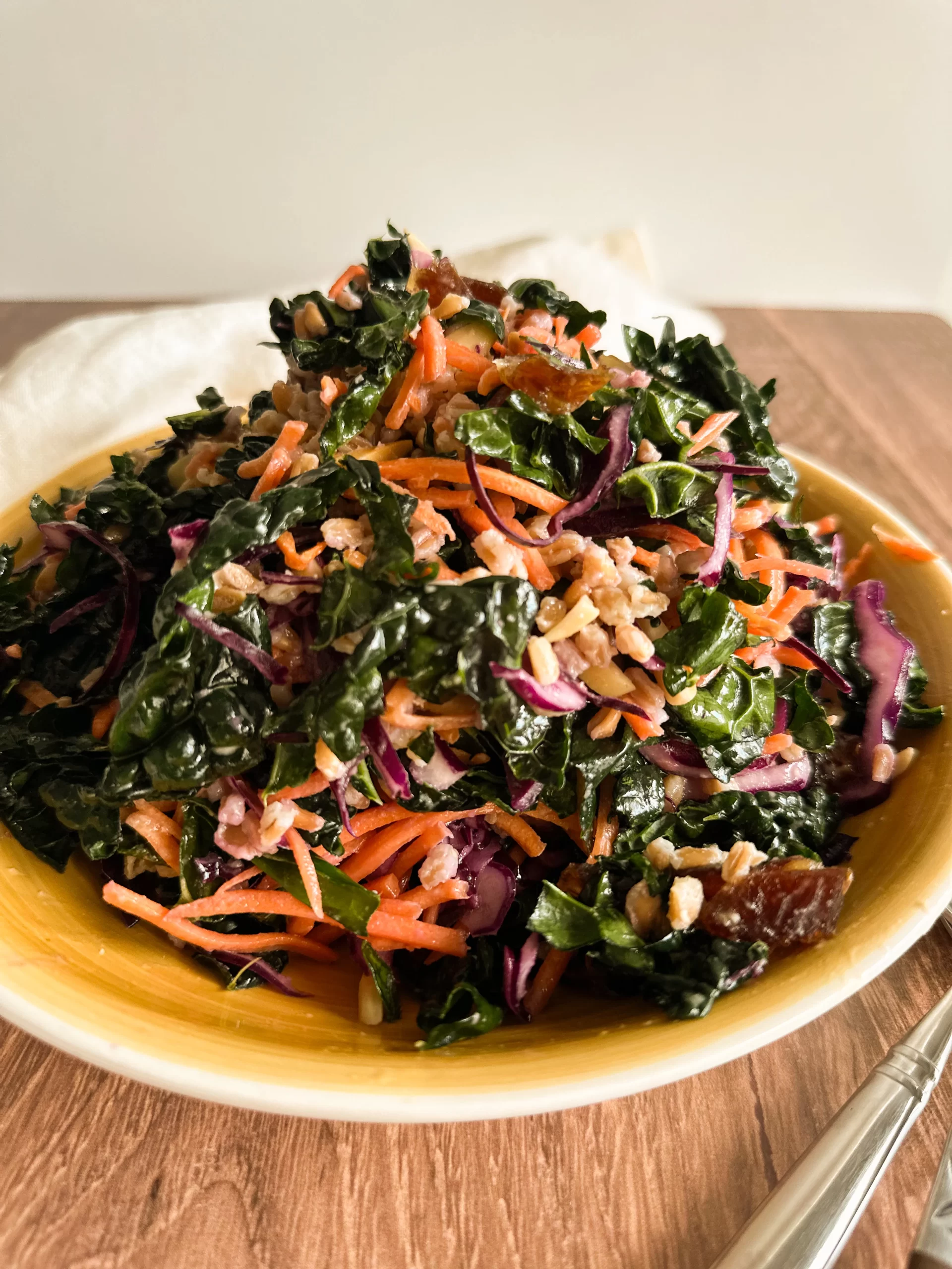 Winter Kale Salad in a yellow bowl on a wood table with a white towel in background