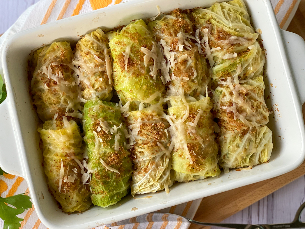 Stuffed cabbage rolls in a white baking dish, topped with Parmesan and Bredcrumbs