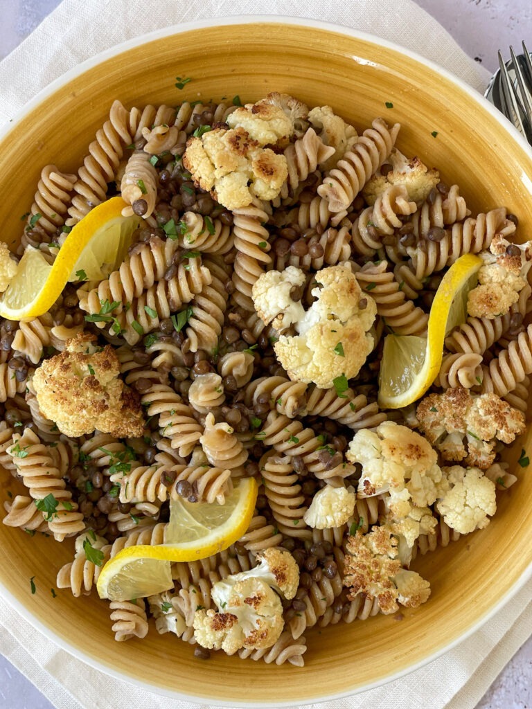 Pasta e Lenticchie with Cauliflower over a white napkins decorated with lemon slices and sprinkled with parsley