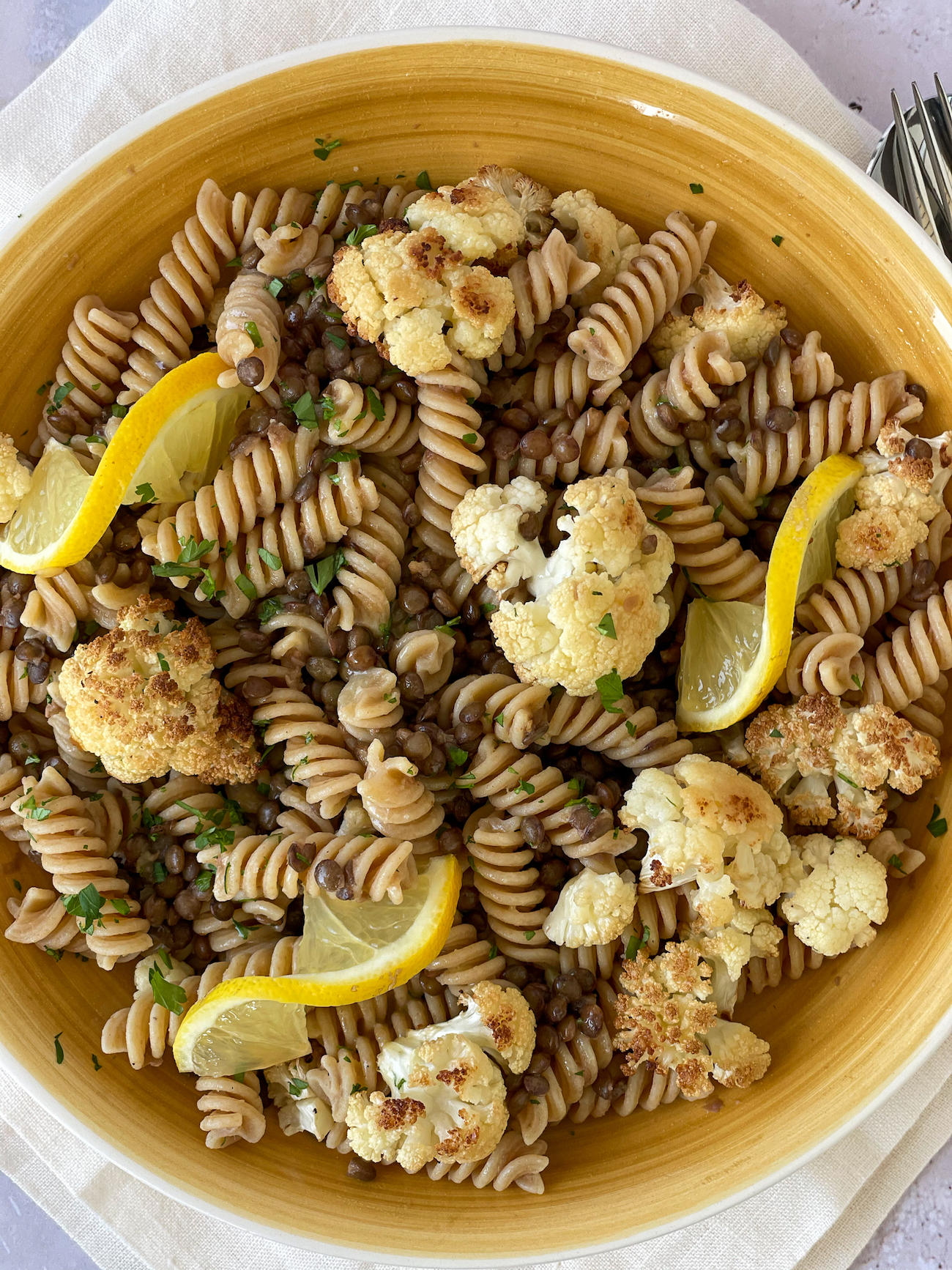 Pasta e Lenticchie with Cauliflower over a white napkins decorated with lemon slices and sprinkled with parsley