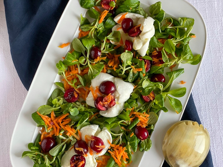 Cherry Buffala Mozzarella Salad over a bed of mixed green leaves and carrots.