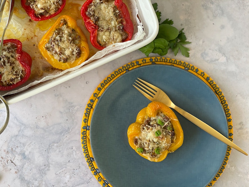 Stuffed Yellow Peppers on a blue plate with baking dish in background.