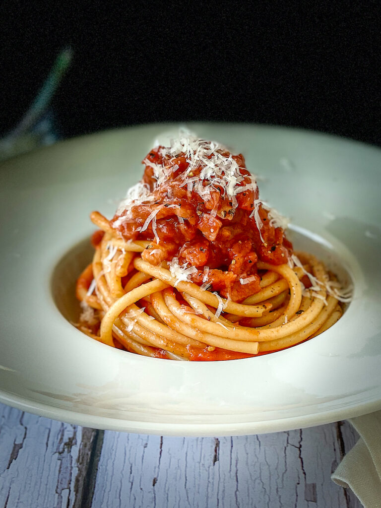 Pasta all'Amatriciana in a white plate with Pecorino cheese on top