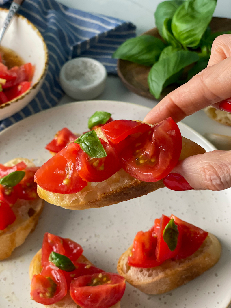Classic Italian Tomato Bruschetta hold in hand on with basil in background