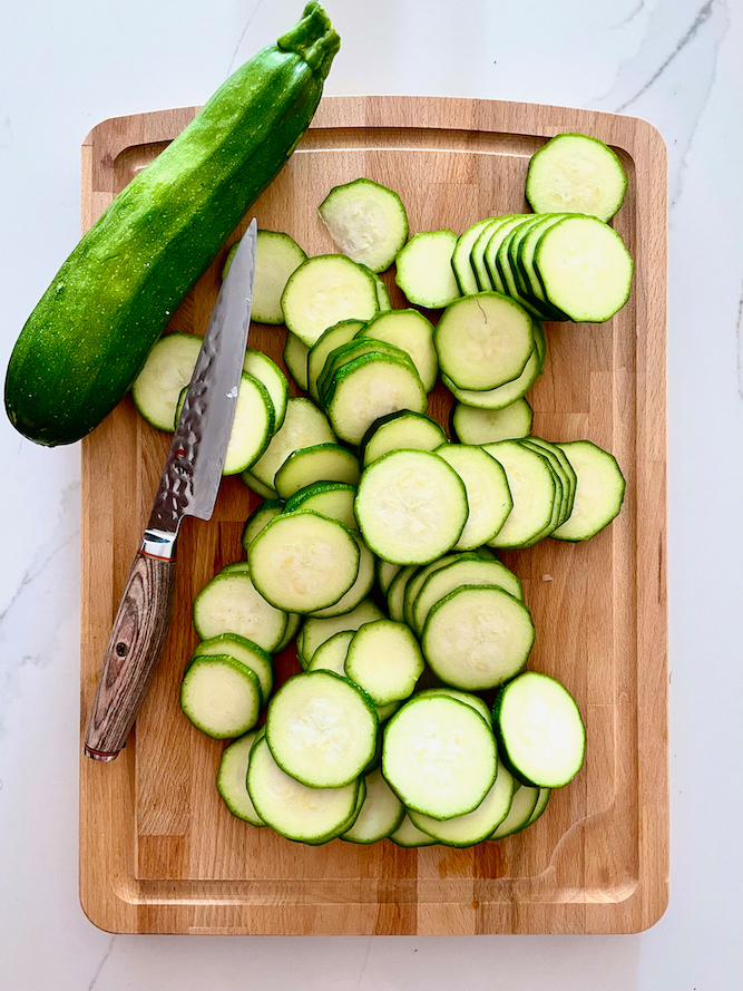 Zucchini sliced with knife over wood chopping board