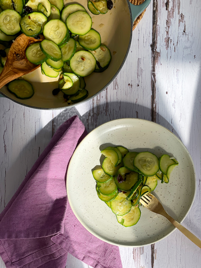 Zucchini with Raisins and Pine Nuts on a white speckled plate with pot in the background