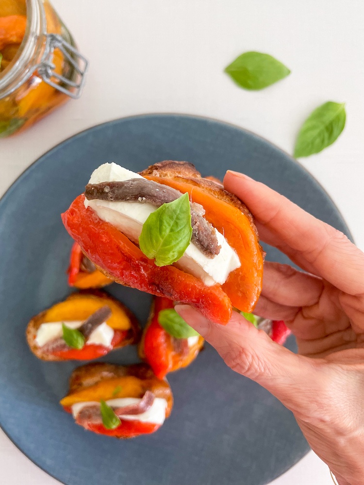 Bruschetta with peppers hold in hand over a blue plate