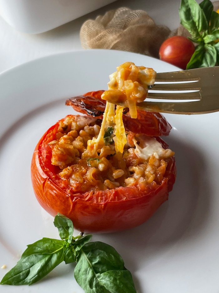 Farro Stuffed Tomatoes on a plate pulling the gooey mozzarella with a fork