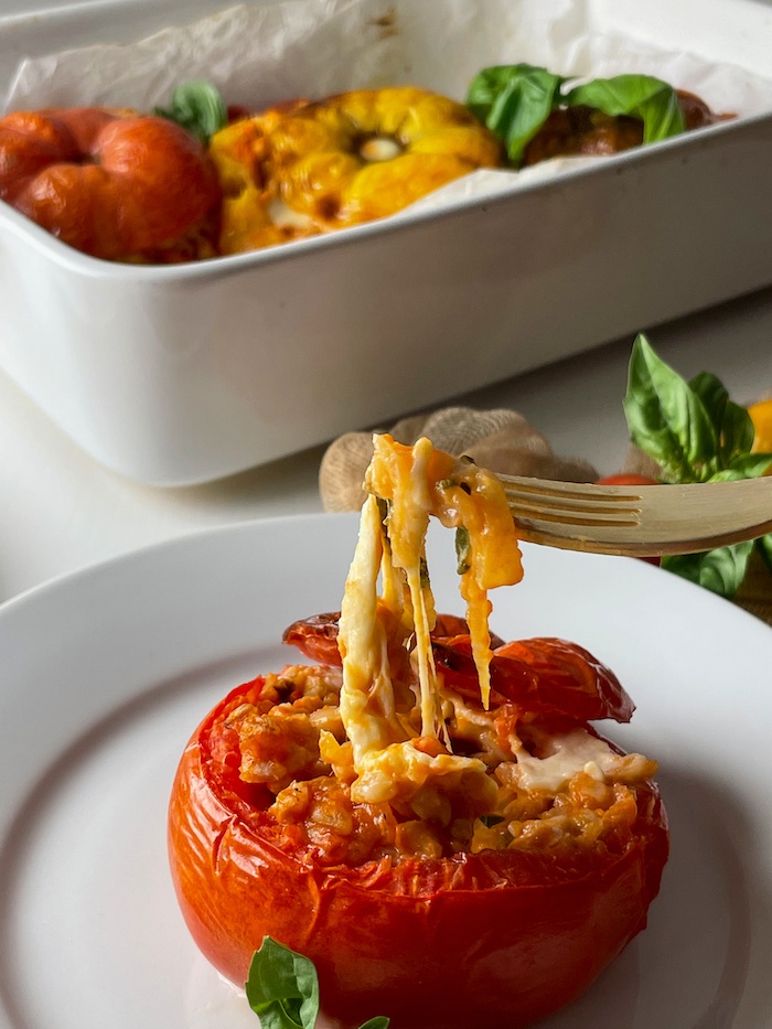 Farro stuffed tomatoes with fork pulling the gooey mozzarella