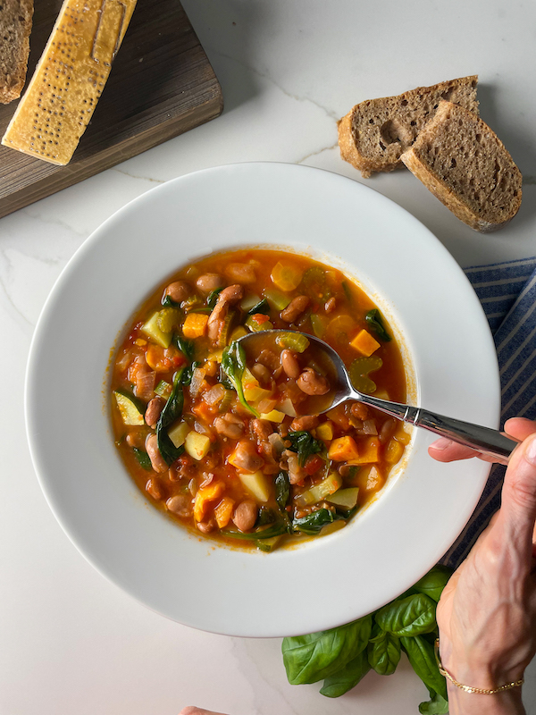 hand holding a spoon of minestrone from a bowl