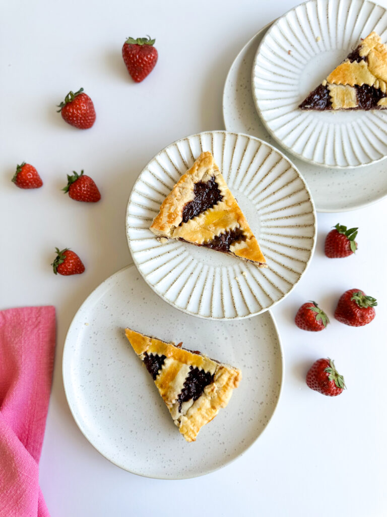 Slices of crostata on white rimmed plate with pink napkin and strawberries