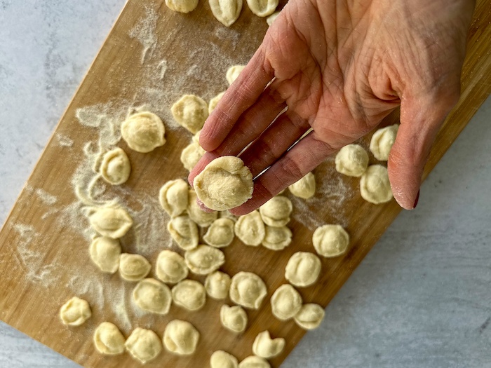 Homemade orecchiette on a wood board with a close up of one in one hand