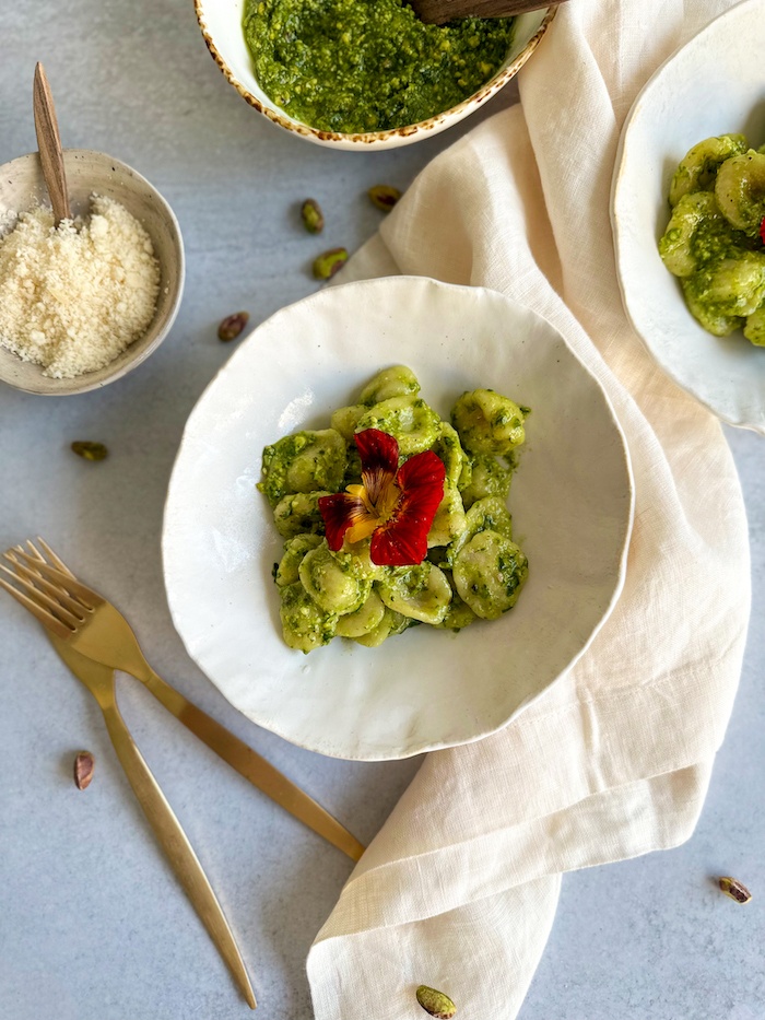 Homemade Orecchiette with wild ramp pesto on a white bowl decorated with a red edible flower.
