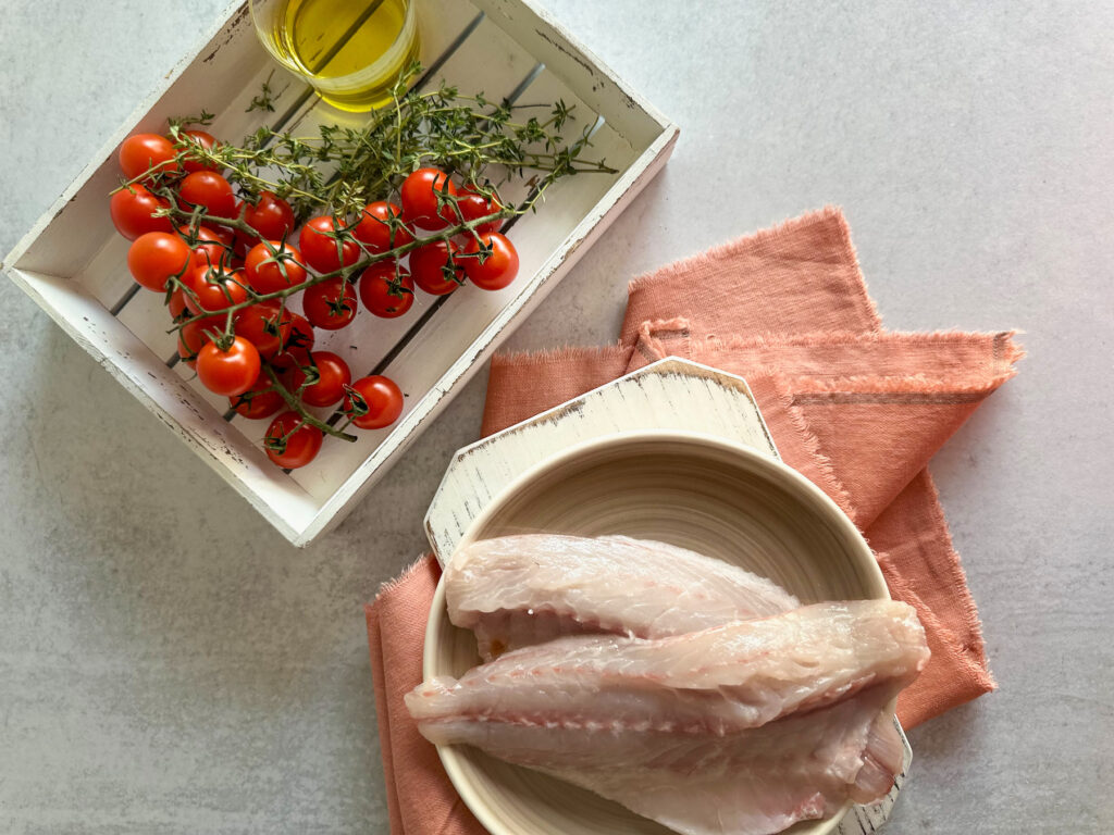 Ingredients for the sea bass ravioli on a table and with tomatoes and thyme in a white wood tray