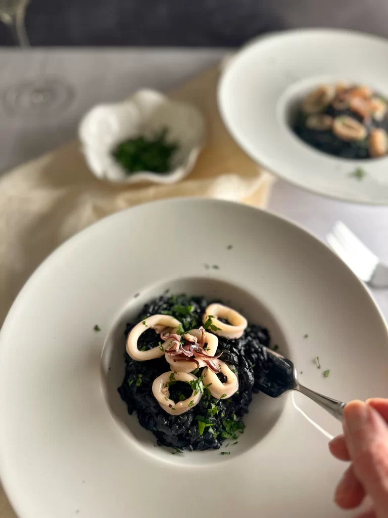 Hand holding a fork, taking a bite of the squid ink risotto