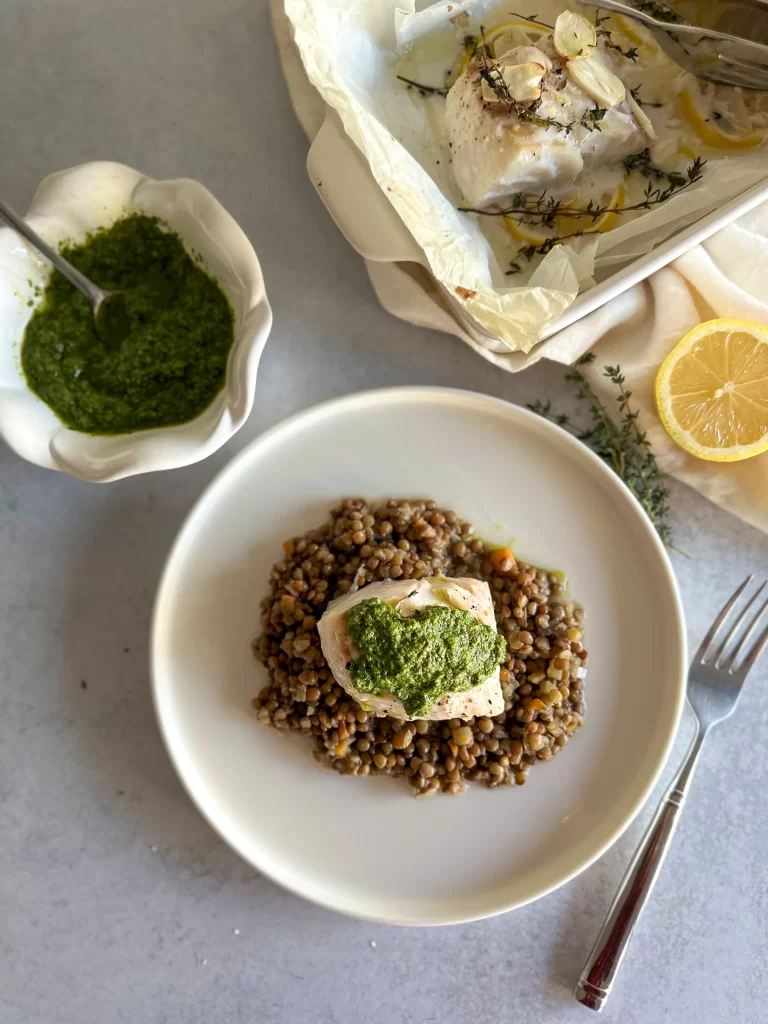 Bakeed Cod over lentils with topping of Salsa verde and a bowl of more salsa .