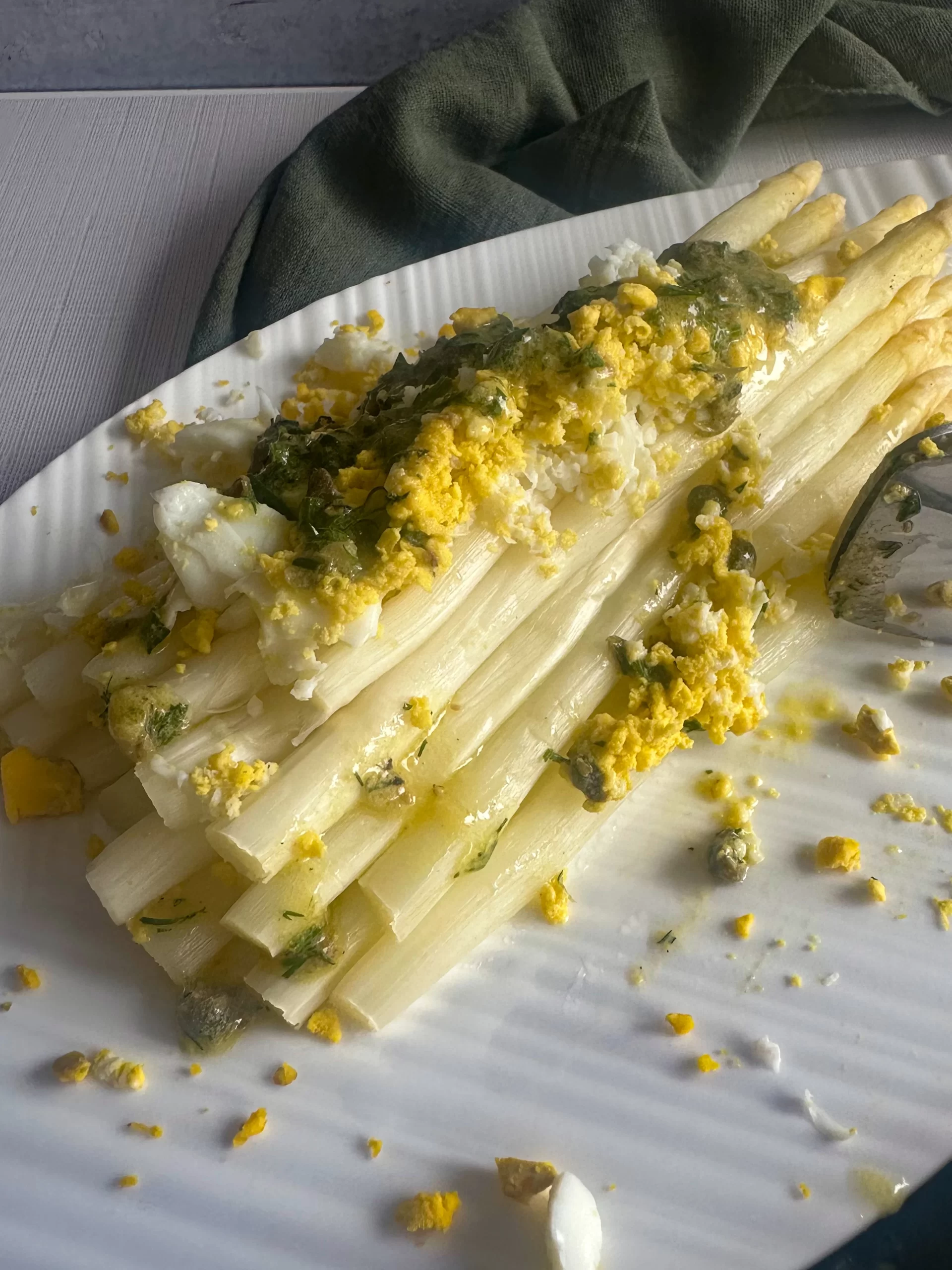 White Asparagus topped with egg and herb capers vinaigrette on a white plate.