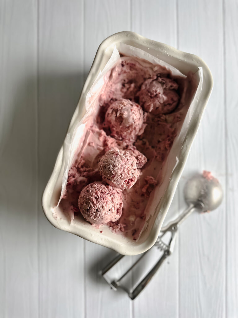 Tray of frozen ice cream with scoops inside and scoops maker on the side