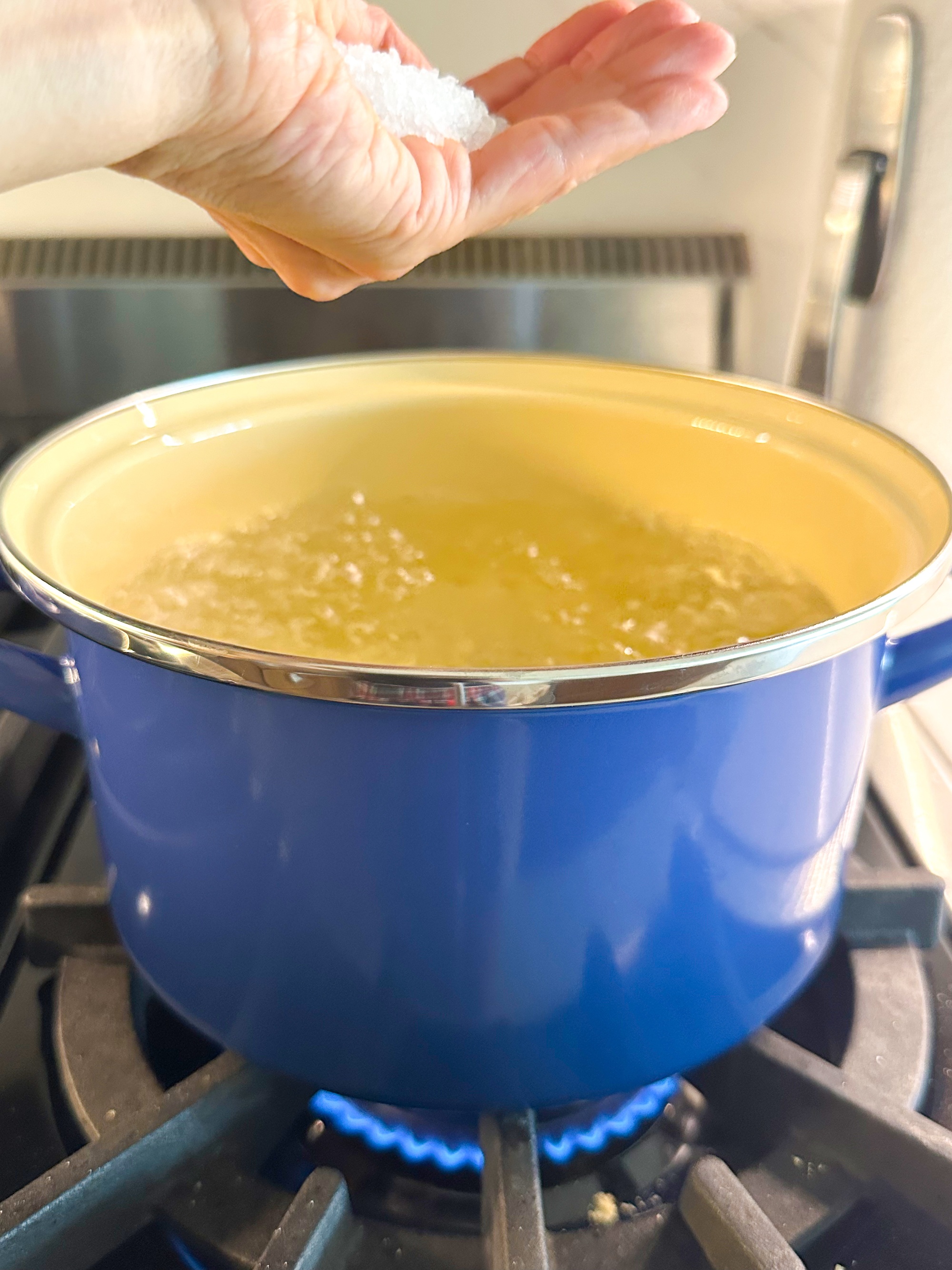 Adding salt to boiling pot of water.