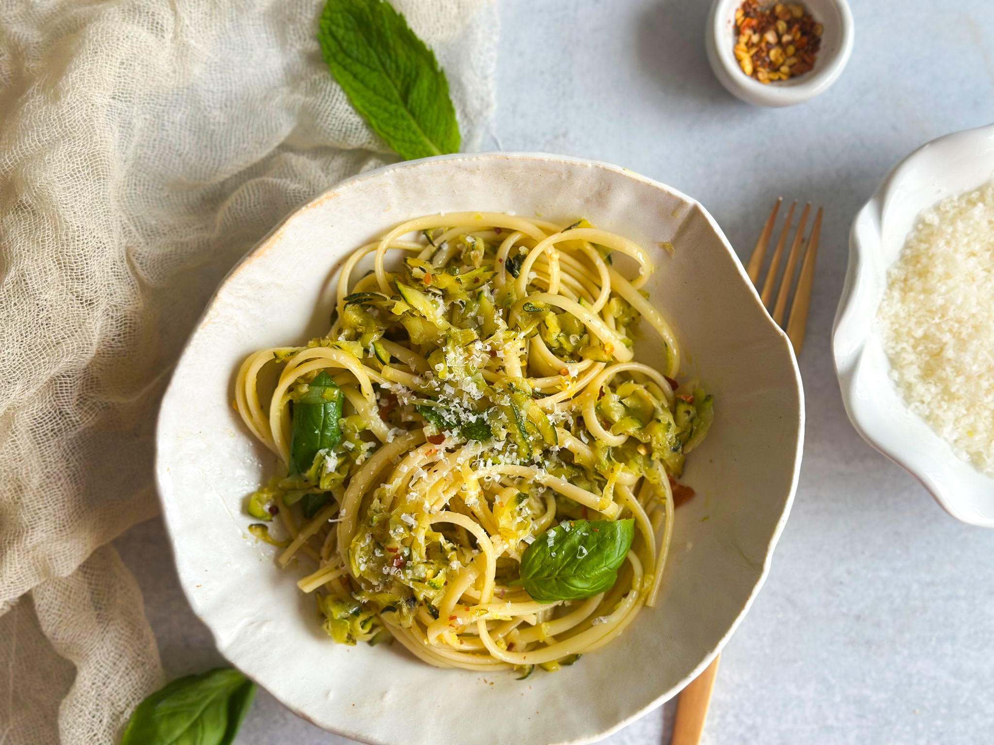 Zucchini pasta in a plate with cheese and red pepper flakes on the side