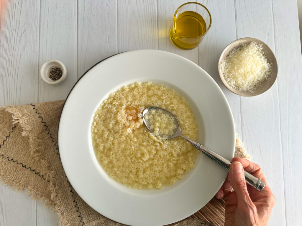 Pastina Soup in a round plate with hands dipping a spoon.